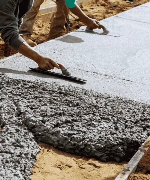 A man laying concrete on a sidewalk, using a hard scraper to smooth the surface.